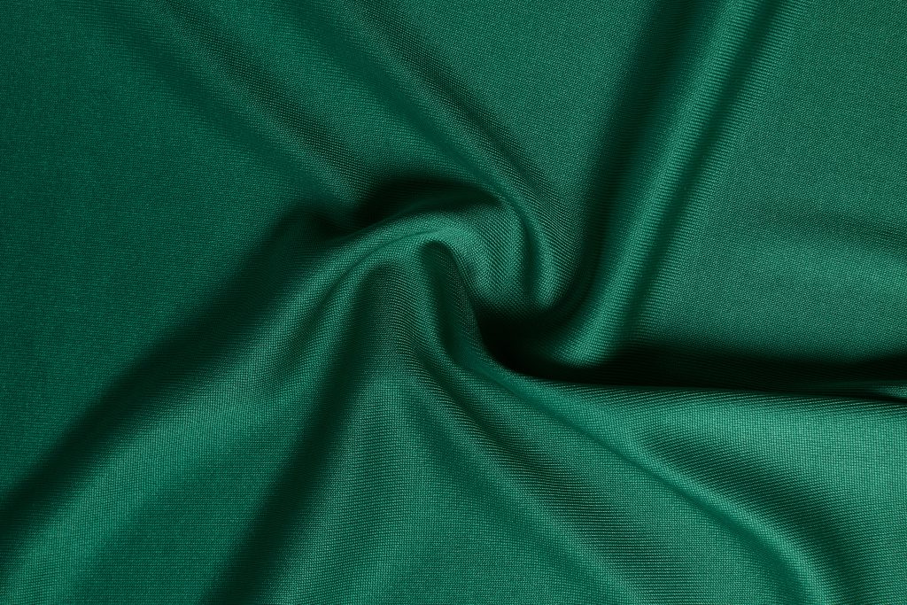 A piece of green fabric showcasing its smooth texture and slight sheen. The fabric is gathered and draped, emphasizing its flexibility and soft, luxurious appearance.