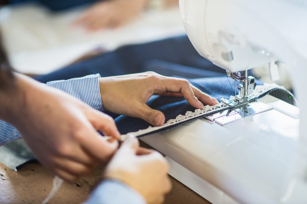 Close zoom on three hands sewing a fabric on a sewing machine.