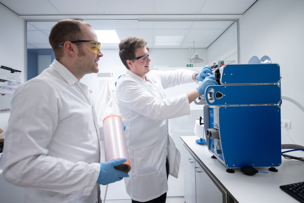 Two Scientists of the NOOSA™ team working on a machine and smiling.