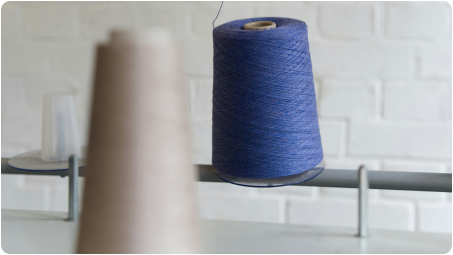 A spool of blue thread on a spindle with a blurred brown spool in the foreground