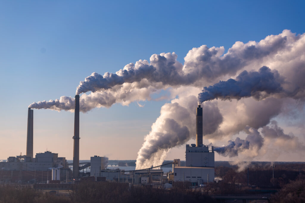 A coal burning power plant with three towers that are emitting clouds of CO² emissions.