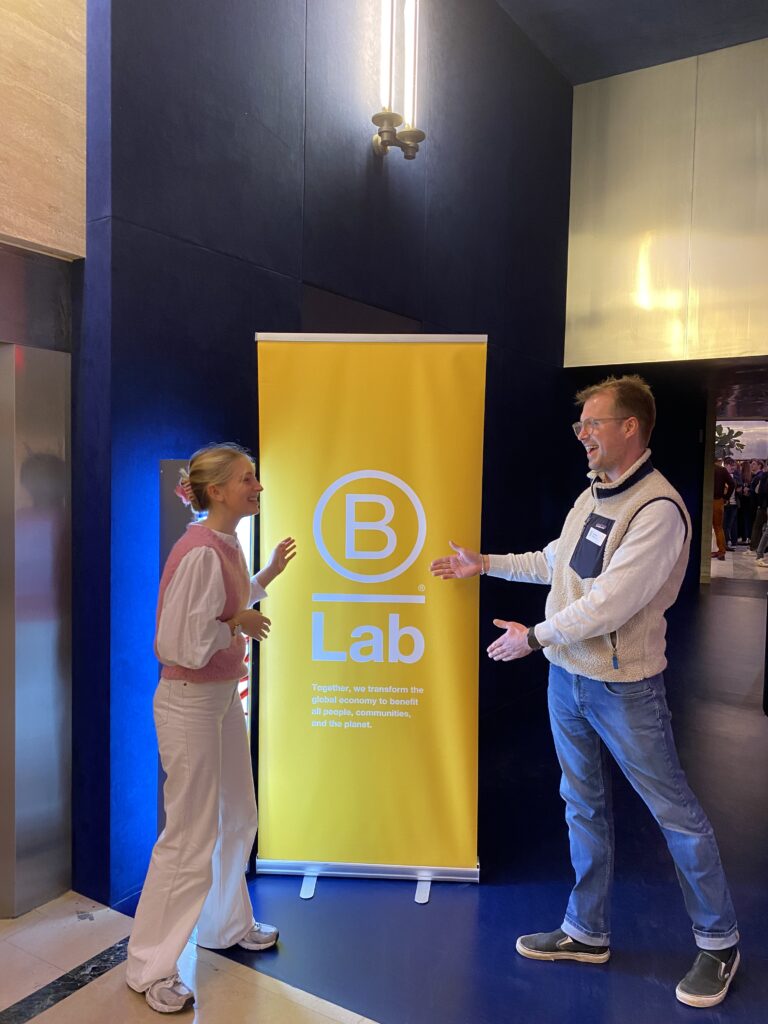 Léa and Jim, two NOOSA™ team members showing a B Lab banner at a B Corp event.