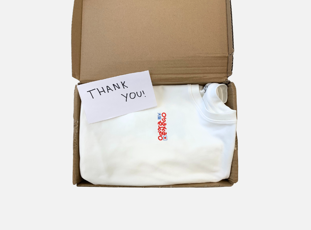 White T-shirt made in NOOSA® fiber packed in a box with with piece of paper that has ¨thank you¨ written on it.