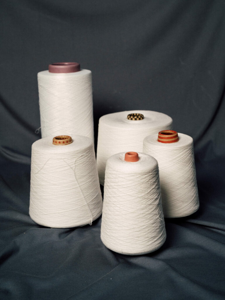 NOOSA® PLA spun and filament yarns bobbins bio based and microplastic free on a blue fabric